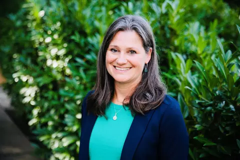 Woman with brown hair wearing a blue blazer and green shirt